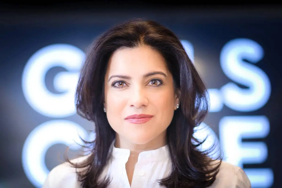 Reshma Saujani, fundadora do Girls Who Code, em um close-up de seu rosto, com o logotipo de sua organização ao fundo, representando sua dedicação à inclusão de mulheres na tecnologia