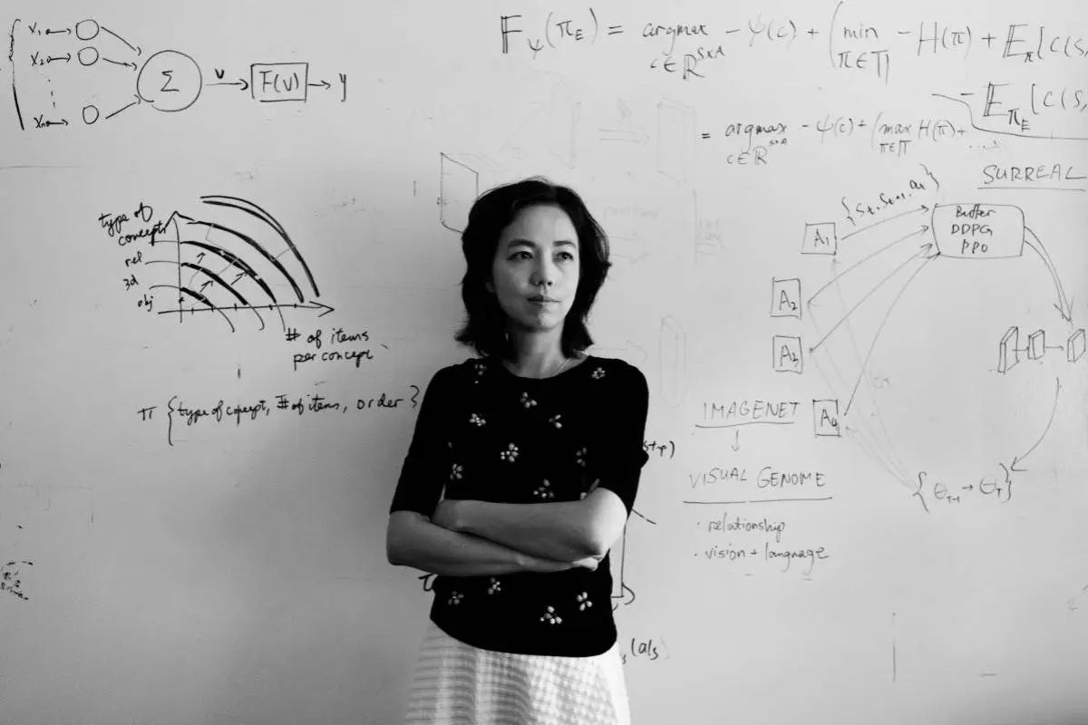 Fei-Fei Li, especialista em inteligência artificial, em pé na frente de um quadro com fórmulas matemáticas e diagramas, representando seu trabalho pioneiro no campo da visão computacional e IA